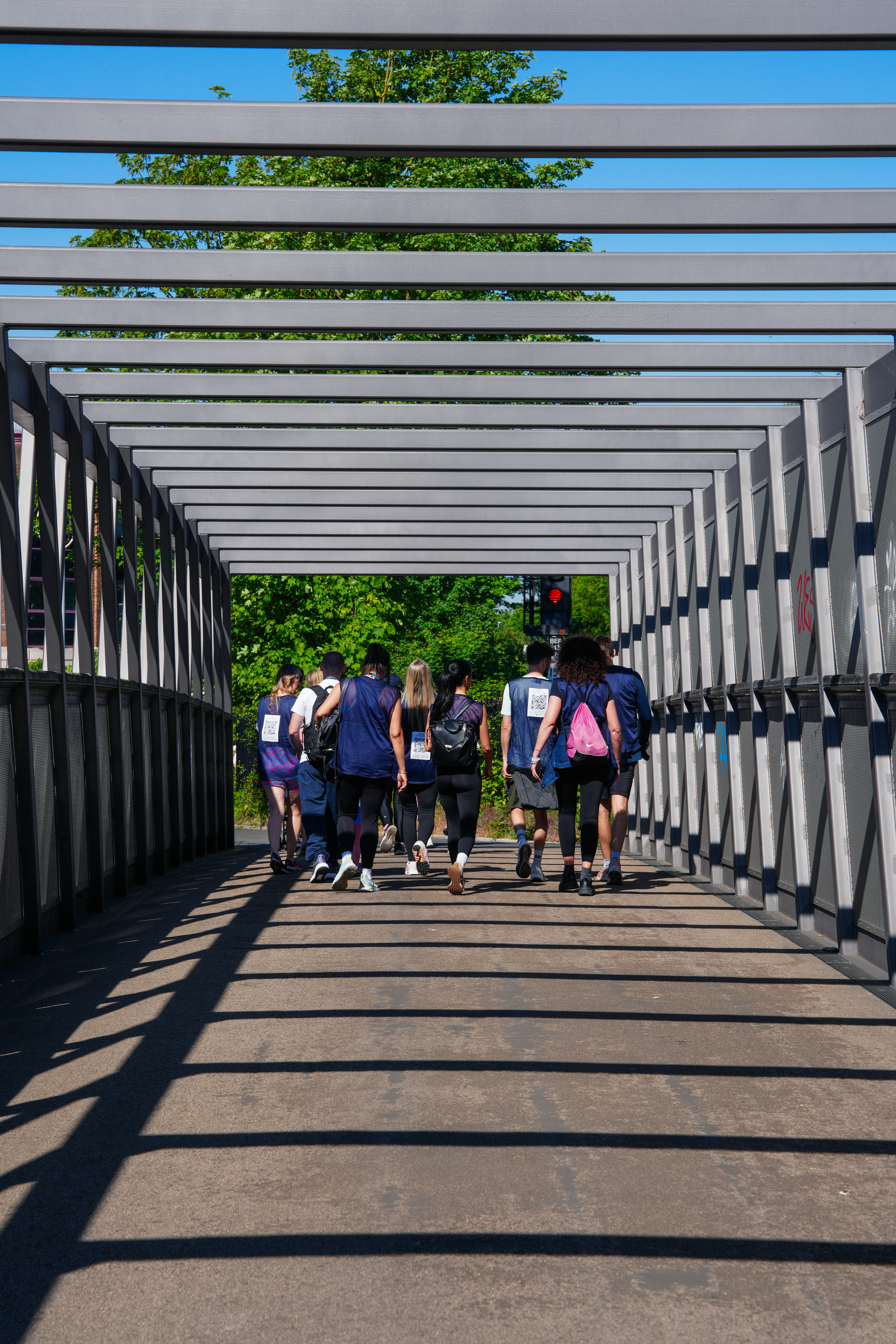 A group of walkers walking along a bridge on the SW London Bridge Walk. QR codes attached to bags and tops to be scanned for donors to donate to Jigsaw4u's children and families.